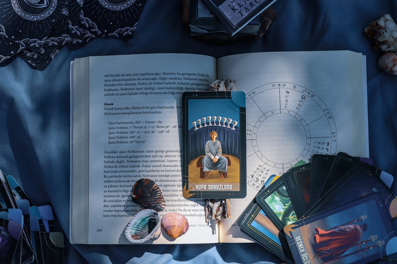 gallery-1 An artistic flat lay of tarot cards and astrology on a book with seashells, featuring Kupa Dokuzlusu card.