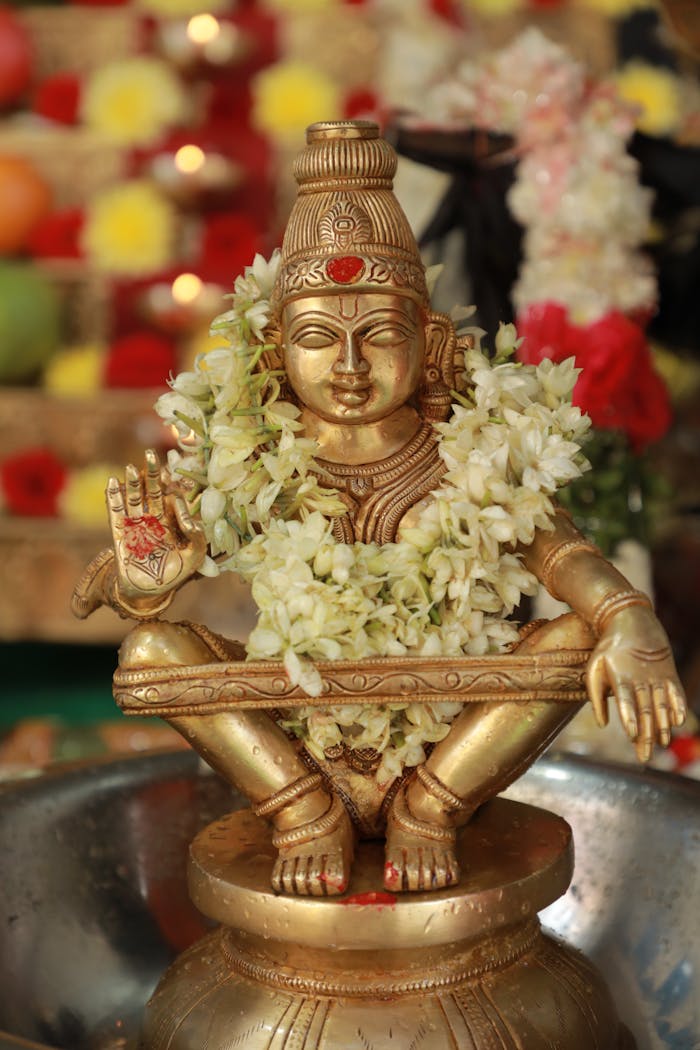 about-02 A golden Hindu deity statue adorned with a white floral garland, symbolizing peace.